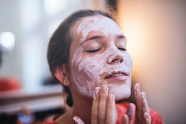 Femme qui s'applique un masque d'argile blanche sur le visage