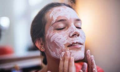 Femme qui s'applique un masque d'argile blanche sur le visage