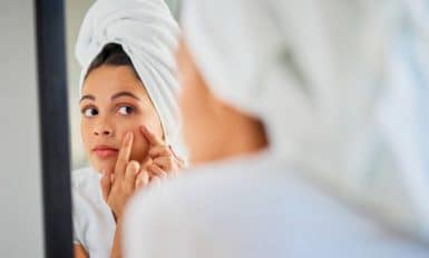 Jeune femme qui examine sa peau dans un miroir